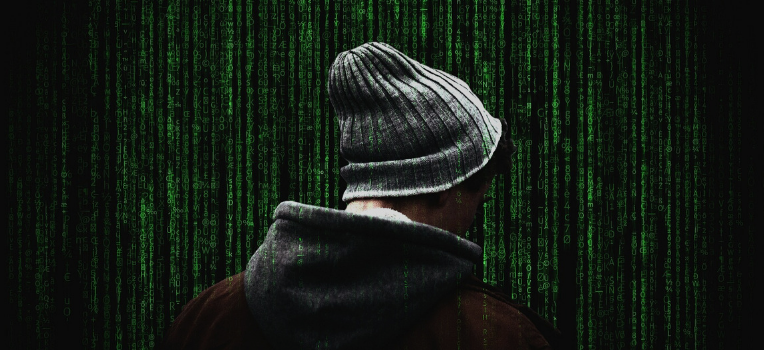 A man wearing a gray beanie and gray hoodie under a dark red or brown coat as shown from behind, shoulders up. In the background are neon green lines of binary code streamining down.