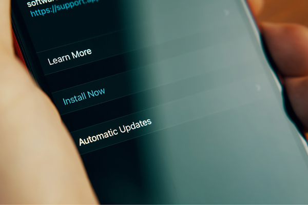 A close-up of a mobile phone, held in someone's hand. On the screen, the user has been prompted to update their software. Options include Learn More, Install Now, or Automatic Updates.